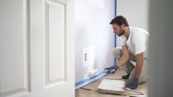 画家の男性は家の中で壁をペイントローラーと白の色の塗料で塗装します 家の部屋の改装 — ストック動画