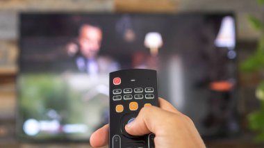 TV kumandasını tutan ve televizyon kanallarını değiştiren bir erkek. Kanal sörfü, ele ve uzaktan kumandaya odaklanmış. İnternet TV.