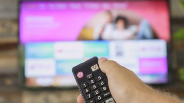TV kumandasını tutan ve televizyon kanallarını değiştiren bir erkek. Kanal sörfü, ele ve uzaktan kumandaya odaklanmış. İnternet TV.