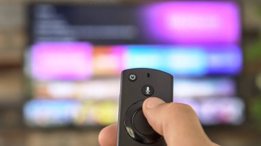 TV kumandasını tutan ve televizyon kanallarını değiştiren bir erkek. Kanal sörfü, ele ve uzaktan kumandaya odaklanmış. İnternet TV.