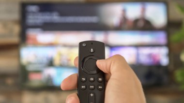TV kumandasını tutan ve televizyon kanallarını değiştiren bir erkek. Kanal sörfü, ele ve uzaktan kumandaya odaklanmış. İnternet TV.