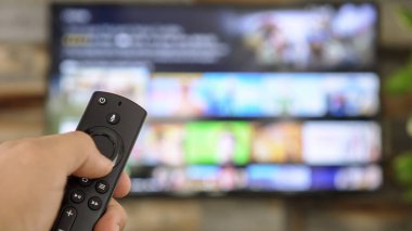 TV kumandasını tutan ve televizyon kanallarını değiştiren bir erkek. Kanal sörfü, ele ve uzaktan kumandaya odaklanmış. İnternet TV.