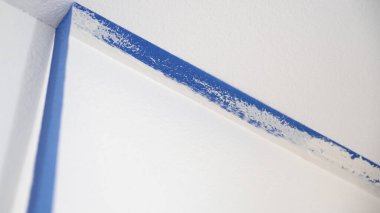 Maske bandını tavandan çıkarıyorum. Bir ressam, duvardan mavi boyacının bandını çıkarıp tavanla temiz bir kenarı ortaya çıkarıyor..