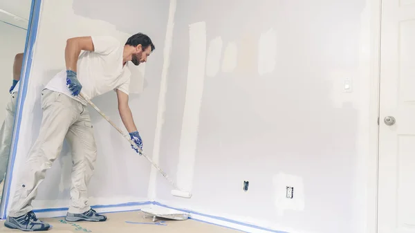 stock image Painter man painting the wall in home, with paint roller and white color paint. Room renovations at house.