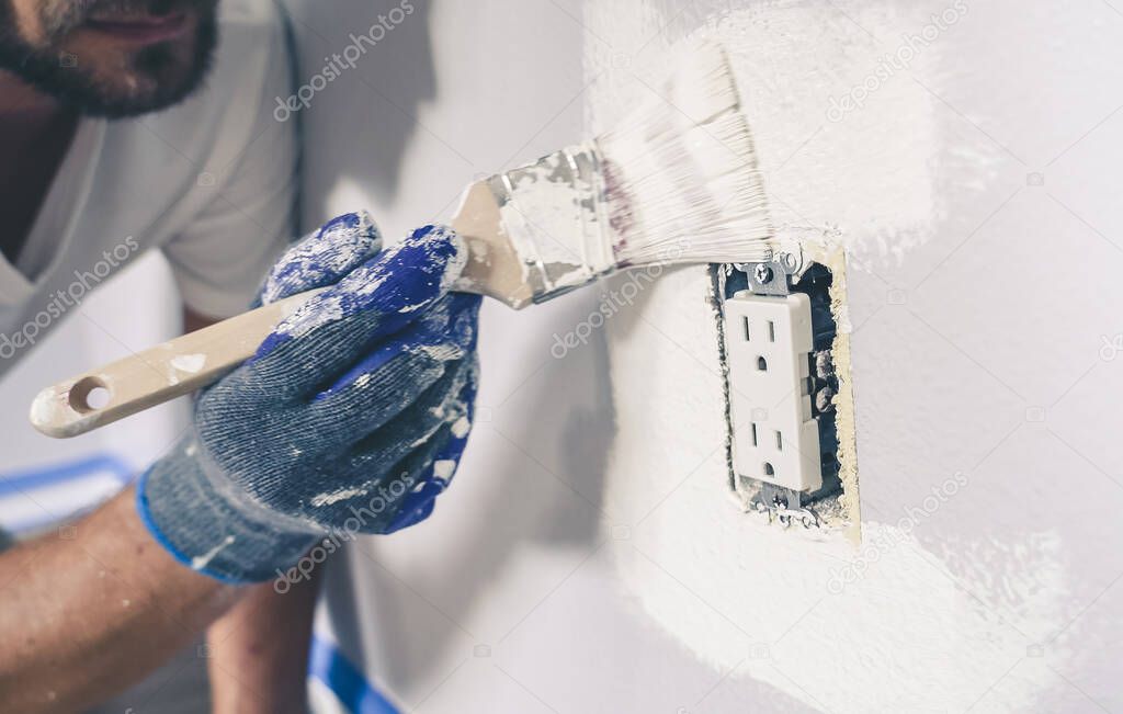Close up of painter man with gloves painting the wall around power outlet.