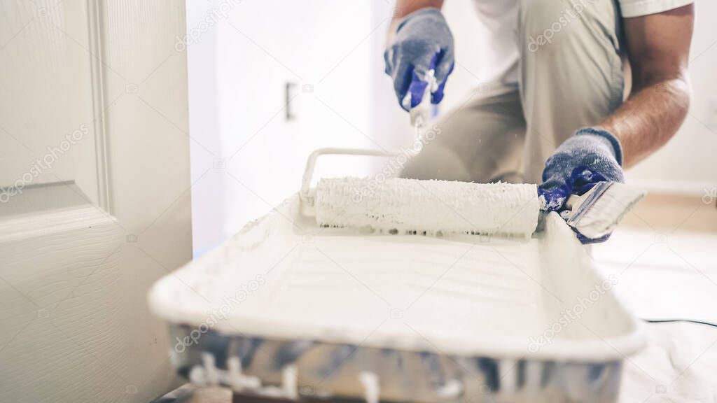 Close Up Shot of White Paint being applied on a Roller. Paint is in the Tray. Room Renovations at Home.