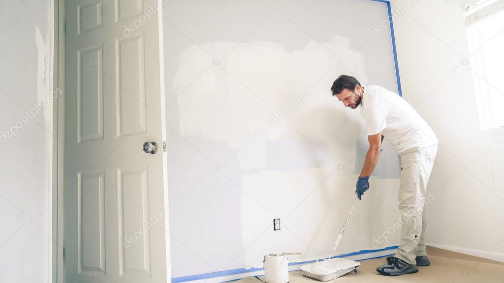 Painter man painting the wall in home, with paint roller and white color paint. Room renovations at house.