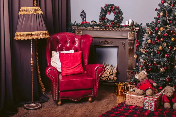 Sillón rojo en un estilo moderno en el interior retro de Año Nuevo con un árbol de Navidad, una chimenea y cajas de regalo — Foto de Stock