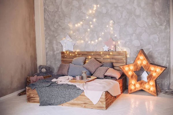 Fából készült ágy található a hálószobában, szép dísztárgyak és egy izzó koszorú — Stock Fotó