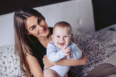 Genç anne ve küçük çocuk bir yatağa oturmuş poz