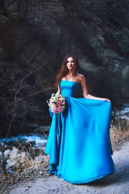 Bir buket çiçek ile mavi bir elbise esmer dağın dibinde duruyor