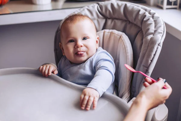 Una chica está tirando de una cuchara con una comida para bebés. Un niño está sentado. — Foto de Stock