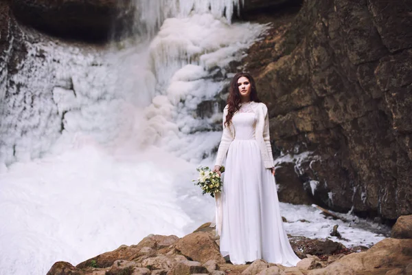 Красивая невеста со свадебным букетом цветов на фоне ледника и гор — стоковое фото