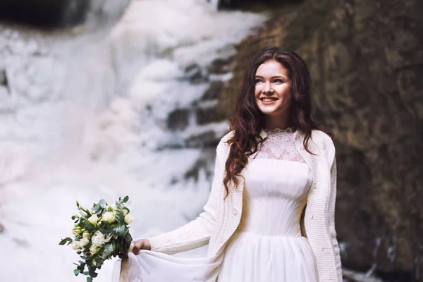 Улыбающаяся девушка в свадебном платье с букетом перед ледником — стоковое фото