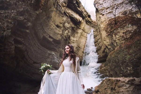 Невеста в шикарном свадебном платье стоит на фоне ледника в горном хребте — стоковое фото
