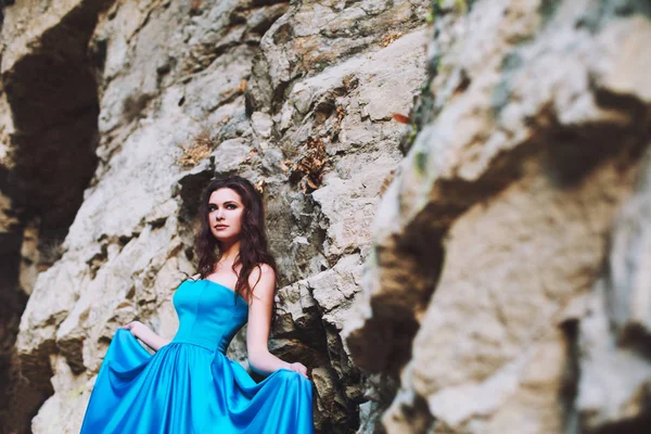 Красивая молодая девушка стоит рядом с горой в синем платье — стоковое фото