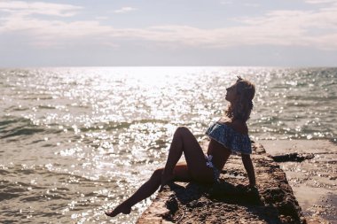 Genç bir kız, güzel mavi bir mayo ve kafasında çiçeklerle rıhtımda poz veriyor..