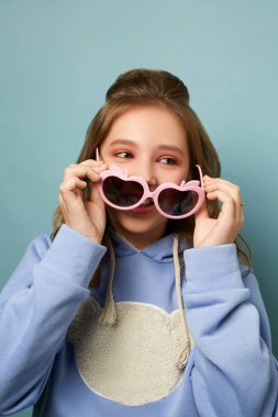Mavi arka planda pembe gözlüklü güzel bir esmer. Stüdyoda poz veren genç çocuk..