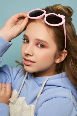 Parlak makyajlı güzel bir genç kız. Stüdyoda mavi arka planda poz veren gözlüklü bir model.