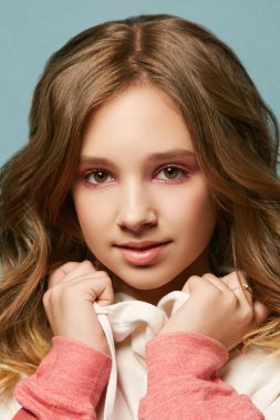 Parlak makyajlı ve saç stili güzel bir genç kız stüdyoda mavi arka planda poz veriyor.