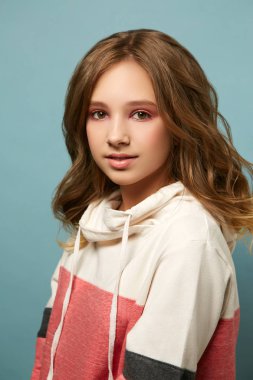 Stüdyoda mavi arka planda poz veren sevimli bir genç. Parlak esmer makyaj.