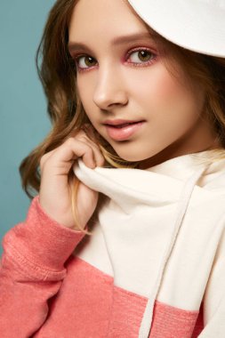 Parlak makyajlı, mavi arka planda süveter ve şapkayla poz veren tatlı bir kız. Güzel yüzlü esmer