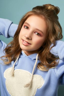 Stüdyoda mavi arka planda poz veren şık saç kesimi olan şık bir kız. Kalın ceketli bir esmerin parlak makyajı..