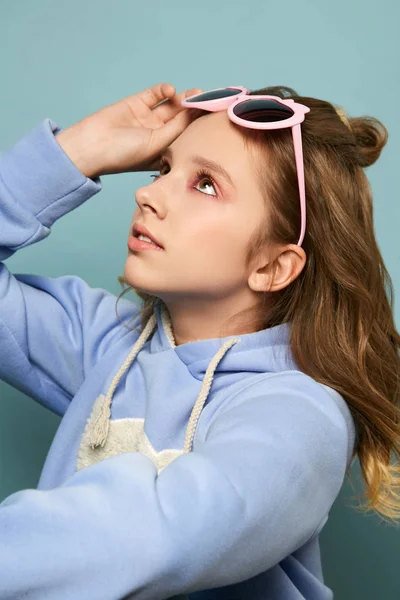 Adolescente linda en gafas de color rosa glamoroso posando en el estudio sobre un fondo azul. Hermosa morena en una sesión de fotos — Foto de Stock