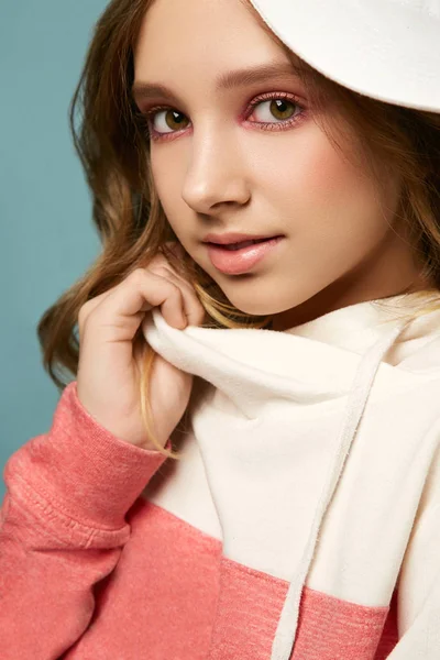 Parlak makyajlı, mavi arka planda süveter ve şapkayla poz veren tatlı bir kız. Güzel yüzlü esmer