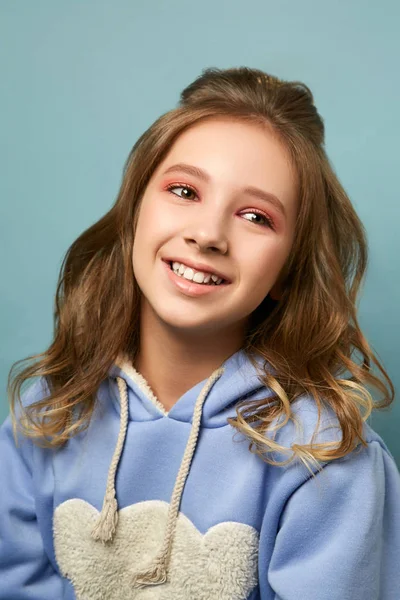 Menina bonito em um fundo azul em uma jaqueta de inverno com um capuz. Morena com um penteado elegante em um estúdio de fotos . — Fotografia de Stock