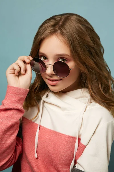 Portret van een stijlvol meisje in glamoureuze glazen die poseren op een achtergrond in de studio. Leuk meisje in een beige jasje. — Stockfoto