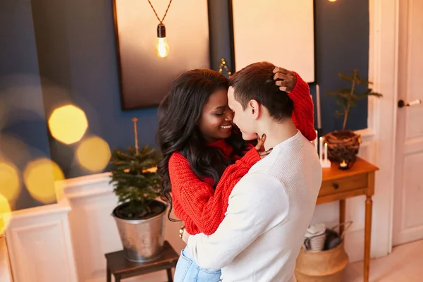 Gli sposi felici festeggiano San Valentino a casa. nero ragazza abbraccia un bianco ragazzo e sorride — Foto Stock