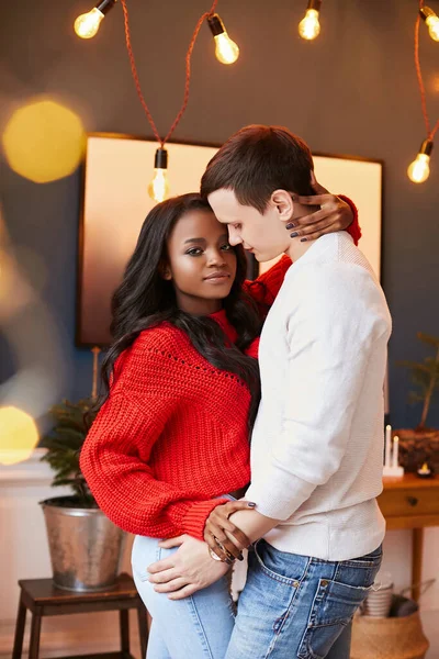 Young interracial couple in love on Valentine\'s day posing while standing at home. Black girl gently hugs a white guy.