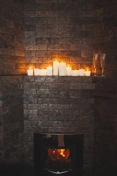 Beautiful modern fireplace with the burning firewood in a stone wall. The burning candles and two glasses for drinks