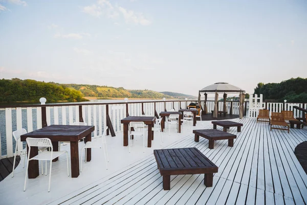 An open-air cafe by the river. Beautiful landscape on low mountains covered with greenery. Wooden tables with chairs and a tent. — 스톡 사진