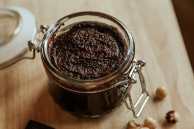 Cam kavanozda ev yapımı çikolata ezmesi ve ahşap bir masada fındık..