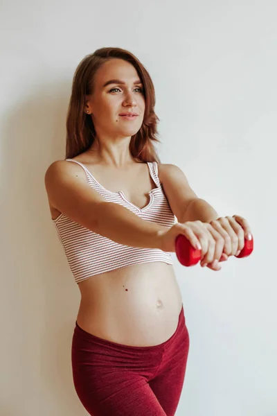 Het meisje is bezig met fitness voor de bevalling. Hef de halter voor je op met je handen. Mooie jonge moeder — Stockfoto