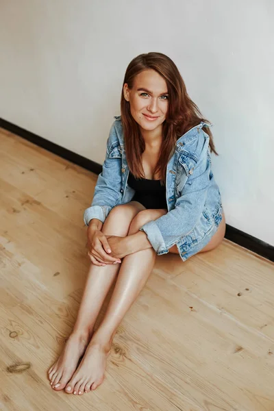 Retrato de uma menina bonito com uma figura luxuosa sentado no chão em uma jaqueta de ganga elegante. Jovem mãe no último mês de gravidez — Fotografia de Stock