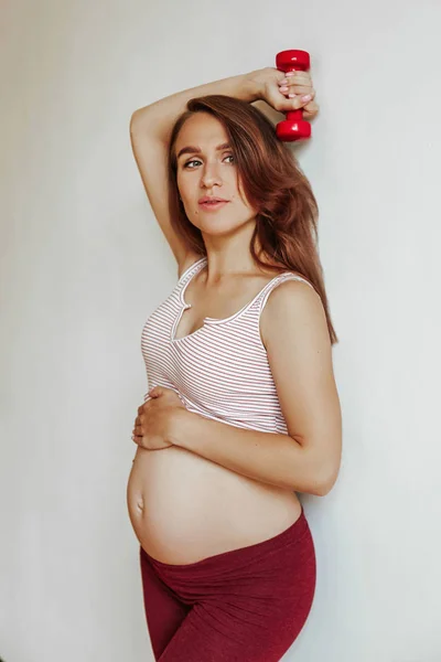 Een zwanger jong meisje tilt een kettlebell over haar hoofd tijdens het sporten. Zwangere vrouw voor de bevalling. — Stockfoto