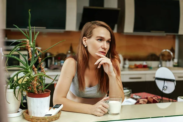 Mladá krásná hnědovlasá žena pije čerstvé mléko z hrnku v kuchyni. Dívka během těhotenství — Stock fotografie