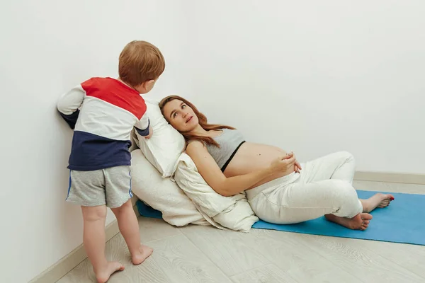 Família jovem. Mãe grávida fala com seu filhinho, apoiando-se em almofadas macias. Menina no último mês de gravidez . — Fotografia de Stock