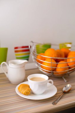 Aromatik kahveli bir kupa ve ahşap bir masanın üstünde taze bir kruvasan..