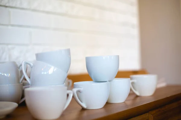 Set of small, white coffee mugs on a wooden tabletop in a cafe.