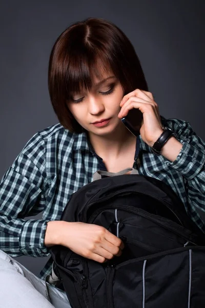 A college student is talking on a cell phone. Brunette girl in casual wear with a backpack.