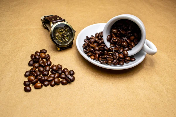 Heart made of coffee a watch and a fallen white cup with coffee beans on a beige background
