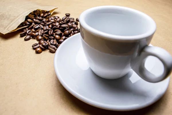 Coffee beans sprinkled from the packaging and a white cup on a beige background