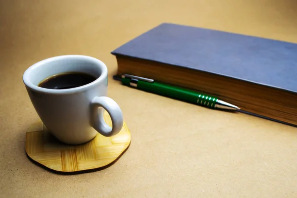 Белая Чашка Кофе Деревянном Подставке Книгой Зеленой Шариковой Ручкой Бежевом — стоковое фото