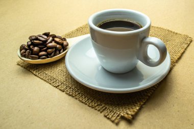 Bir fincan kahve peçetede, yanında da bir kaşık kahve çekirdeği.