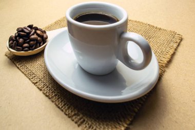 Bir fincan kahve peçetede, yanında da bir kaşık kahve çekirdeği.