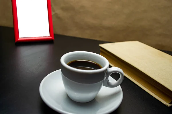 Cup of coffee with a book and a photo frame on a black table